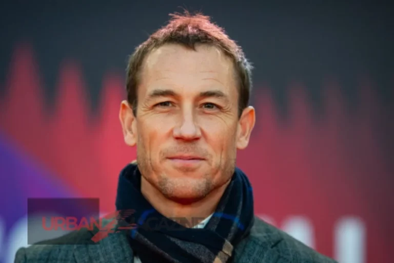 Tobias Menzies Net Worth & his smiling in a suit, representing and successful acting career in TV shows like Outlander and The Crown.